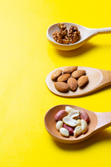 three Spoons with hazelnuts, walnuts, almonds on yellow paper