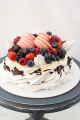 Pavlova cake with whipped cream, raspberry, blueberry, blackberry and french macaroons. Copy space, plain background.