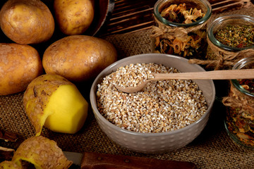 barley on wooden spoons, dried plums next to one peeled potato and dried mushrooms next to dried spices