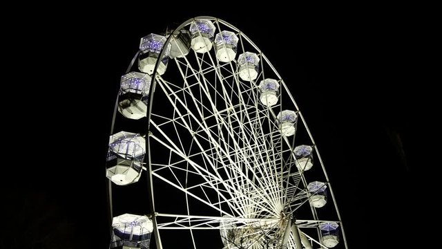 4K: Ferris Wheel lit up at night in the dark evening skay. The big round circle rotates and is illuminated. Side view. Stock Video Clip Footage