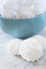 White meringues in the blue ceramic bowl and three meringues nearby with reflection in the bowl on the wooden rustic table close up. Vertical format