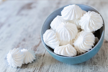 Fototapeta na wymiar Small white meringues in the blue ceramic bowl and two meringues nearby on the wooden rustic table
