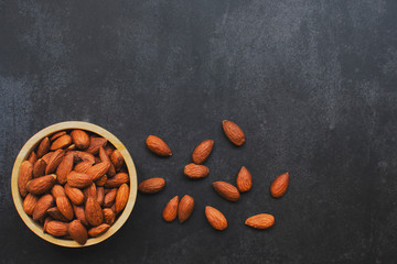Top view of almonds in wooden bowl. Nuts freely laid on dark background.