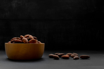 Aalmonds in wooden bowl. Nuts freely laid on dark background.