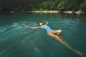 traveler carefree woman relaxing and floating in calm clear water, swimming on back in blue lake. Outdoor adventure, people in nature and calmness concept