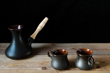 Two black cups for coffee and black turk on the old wooden table and black background. Cozy home idea. Sweet home
