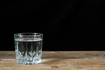 Glass of water on wooden table with black background