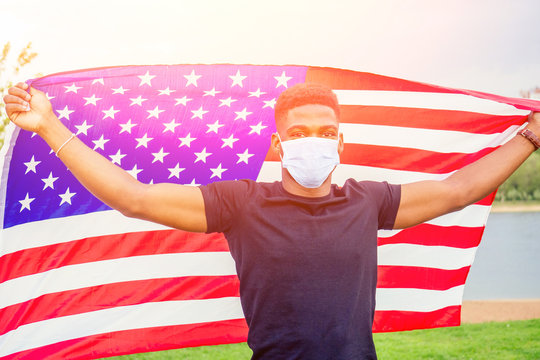 Handsome afro american man with united states flag in hands in summer park near lake evening