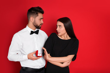 Young woman rejecting engagement ring from boyfriend on red background