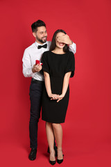 Man with engagement ring making marriage proposal to girlfriend on red background