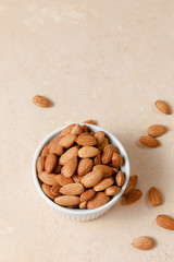 Almonds in white porcelain bowl on beige background.