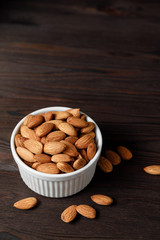 Almonds in white porcelain bowl on wooden table.