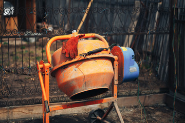 Orange concrete mixer at the construction site, foundation tools