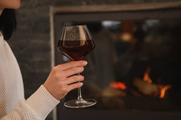 Woman with glass of wine near burning fireplace, closeup. Space for text