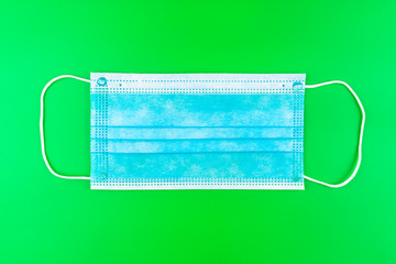 Disposable blue surgical mask, isolated on a green background, top view.