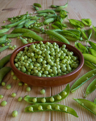 Green peas in bowl on rustic wooden background, natural wooden table