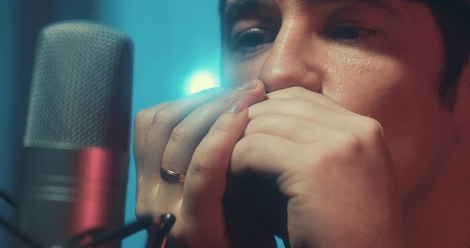 Close-up Musician in headphones playing on harmonica at home sitting on floor at evening time. Music hobby, Create own songs, learning online. Social distancing, 4K video
