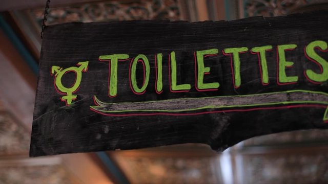 Pan shot of text of toilettes written on blackboard with colorful chalk in french language denoting toilet with arrow mark and unisex pattern