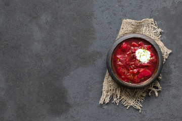 Beetroot soup with greens and sour cream in a wooden bowl on a linen napkin on a dark gray...
