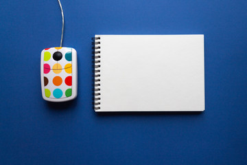 White computer mouse with color dots and spiral notebook on trendy classic blue background. minimal style. top view