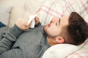 Sick young man sneezing at home. Influenza virus