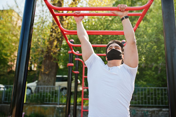 Fototapeta premium Portrait sports arabian man in black medical face mask doing workout exercises in outdoor gym place during coronavirus quarantine.