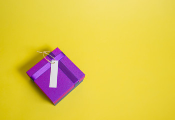 A closed gift box with an empty price tag on a yellow background. Purple gift box. Sale ads