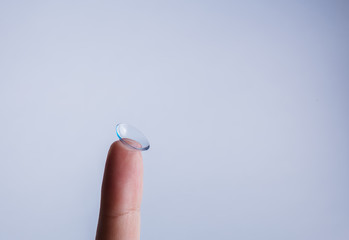 Transparent lens on the finger on a white background with free space. Myopia, vision problems.