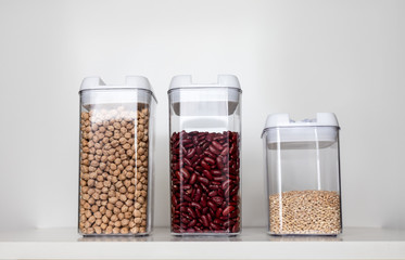 Three Clear Pantry Containers on a Shelf Filled with Non-Perishable Foods-- Dried Beans and Grains