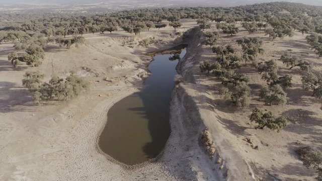 AERIAL DRONE ORBIT OF BIG PUDDLE OF WATER AND MUD SURROUNDED BY ARID FIELDS OF OAKS 