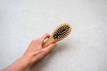 The woman 's hand holds a massage hair comb. Top view beauty tool on concrete gray background.