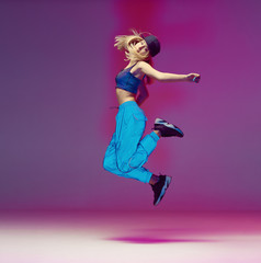 Cute teen girl dancing hip hop in reflective pants, baseball cap, in a Studio with neon lighting....