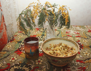 A bowl with olivier salad, a cup of tea and a bouquet of mimosa flowers on a table covered with a colored tablecloth.