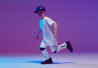 Cool young boy child dancing hip hop in the Studio against the background of neon lights. Break...