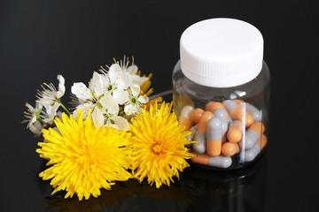 Pills in a bottle and fresh spring flowers, medication in capsules on a dark glass table. Concept of herbal medicine, pharmacy, natural vitamins