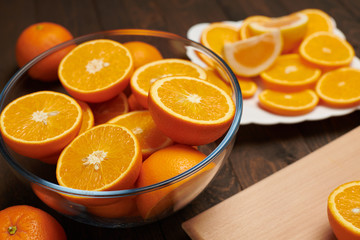 Fresh orange fruit whole and sliced on a wooden table, cutting board and kitchen knife. A plate full of citrus slices - natural and healthy food. Glass of fruit cocktail.