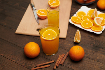 Fresh orange fruit whole and sliced on a wooden table, cutting board and kitchen knife. A plate full of citrus slices - natural and healthy food. Glass of fruit cocktail.