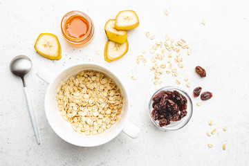 Bowl of oatmeal for porridge with ingredients banana, honey and raisins on white background, healthy breakfast every day, diet food