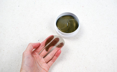 Hydrogel eye patches with gold in a container isolated on a white background. Women 's hand holds...