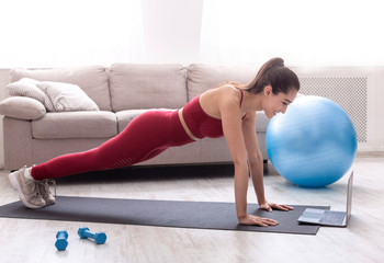 Strength training at home. Fit millennial woman doing plank exercise or push ups to video class in...