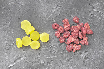 yellow candies compare to dried cranberries on grey background. sugar substitution concept. eating...
