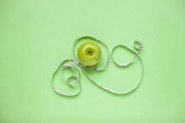 Diet and healthy eating concept. Top view of weightloss. Green apple and measuring tape. Green background