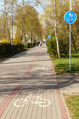 City sidewalk with track of bike lane, white bicycle sign on road and blue road sign with bike and pedestrians.