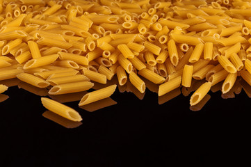 Penne pasta on a black mirror with reflection.