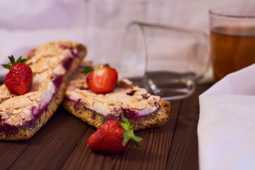 Wooden dark background of planks, white cloth, glasses with tea and homemade pie with cherries and strawberries. Delicious pastries for breakfast.