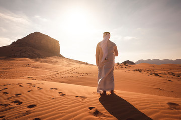 Arab man stands alone in the desert and watching the sunset. - obrazy, fototapety, plakaty