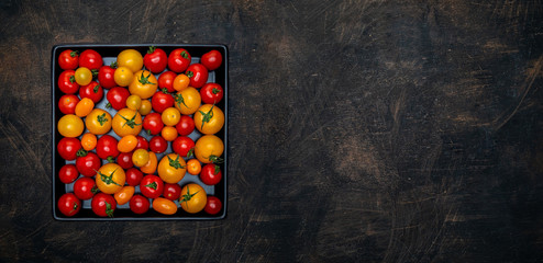 Pile of fresh red and yellow cherry tomatoes in black ceramic tray on vintage table. Overhead shot with copy space.