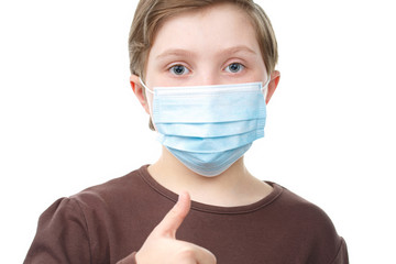 Child in medical mask shows thumb up.