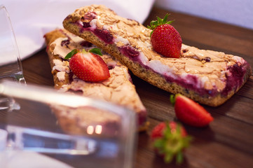 Wooden dark background of planks, white cloth, glasses with tea and homemade pie with cherries and strawberries. Delicious pastries for breakfast.