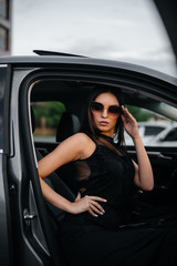 Fototapeta na wymiar Stylish young girl sitting in a business class car in a black dress. Business fashion and style